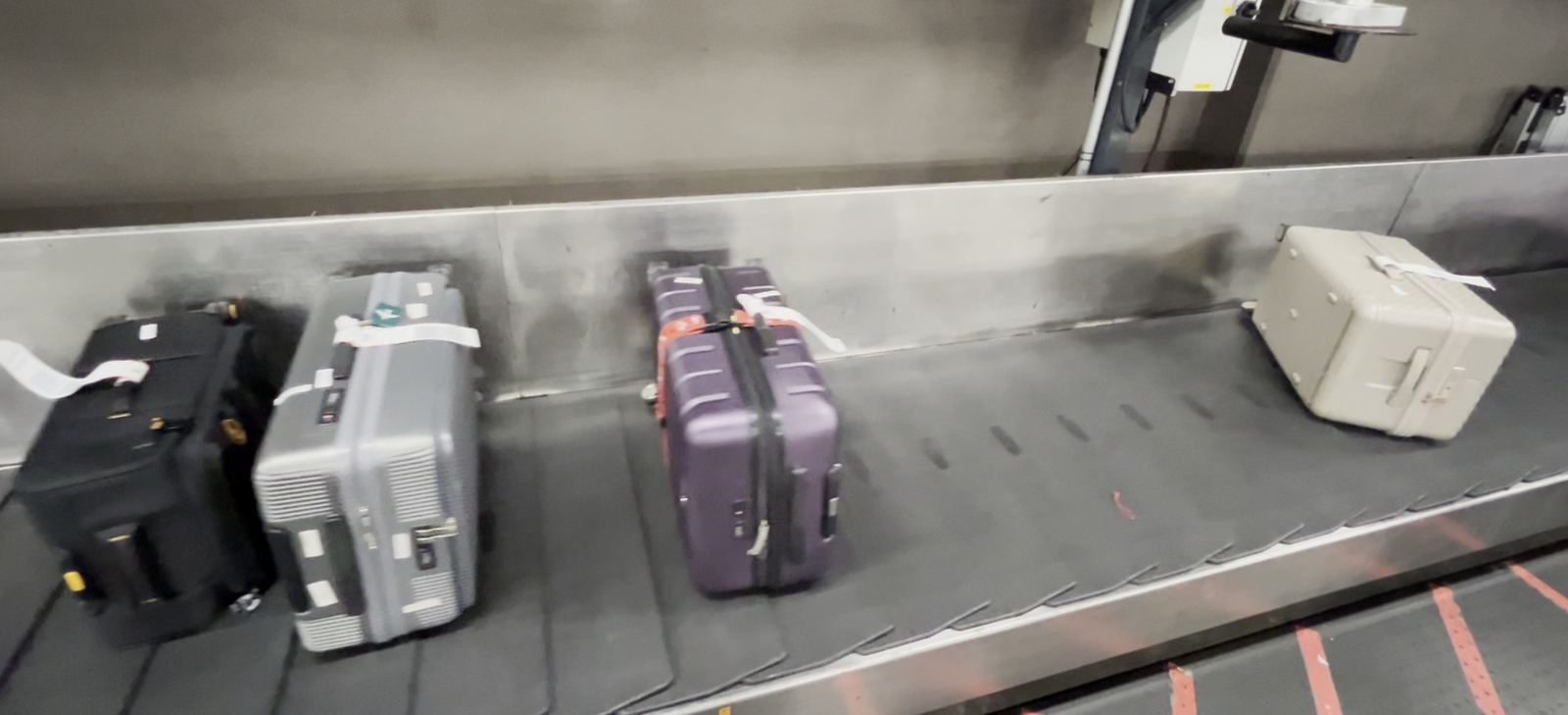 Narita, a live baggage line. The first two cases are touching, the third has a hand's width of gap, the fourth is metres downstream. Nothing on any of them says which is which