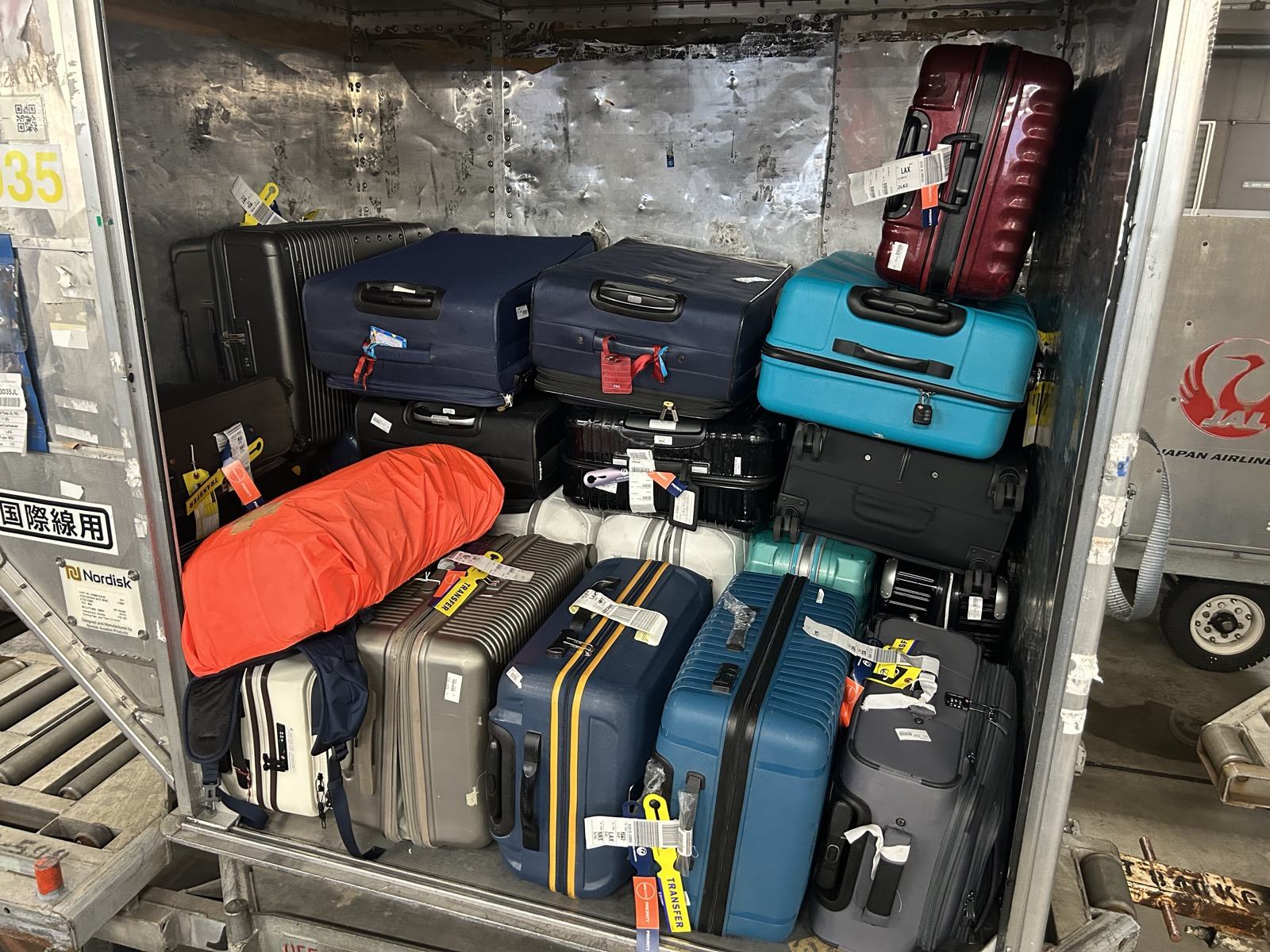 A JAL cargo container packed at Narita: the population this line has to survive, hard shells, fabric, vinyl-wrapped, leather-trimmed, no two the same size